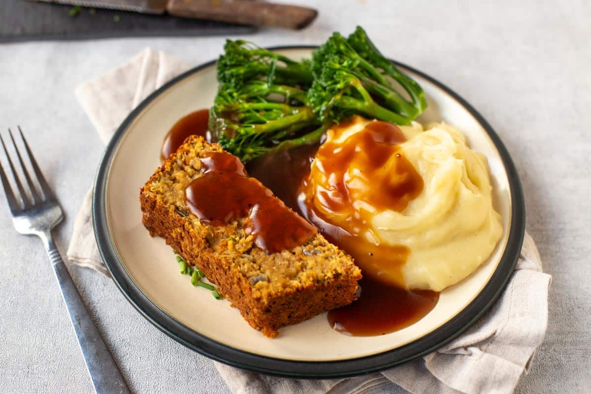 A slice of vegan lentil loaf with mashed potato, broccoli and gravy.