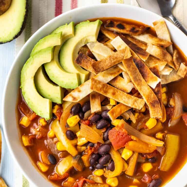 Vegan taco soup in a bowl topped with avocado and tortilla strips.