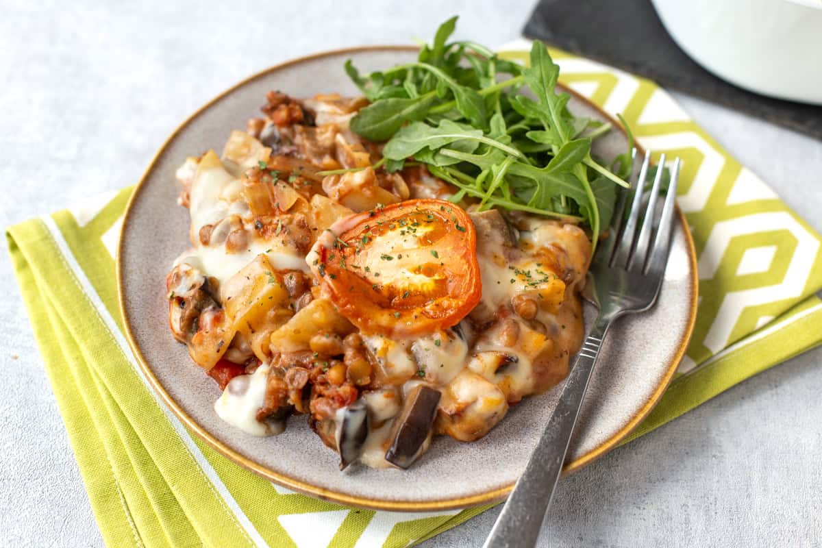 A portion of vegetable moussaka with lentils and eggplant, topped with sliced tomato.