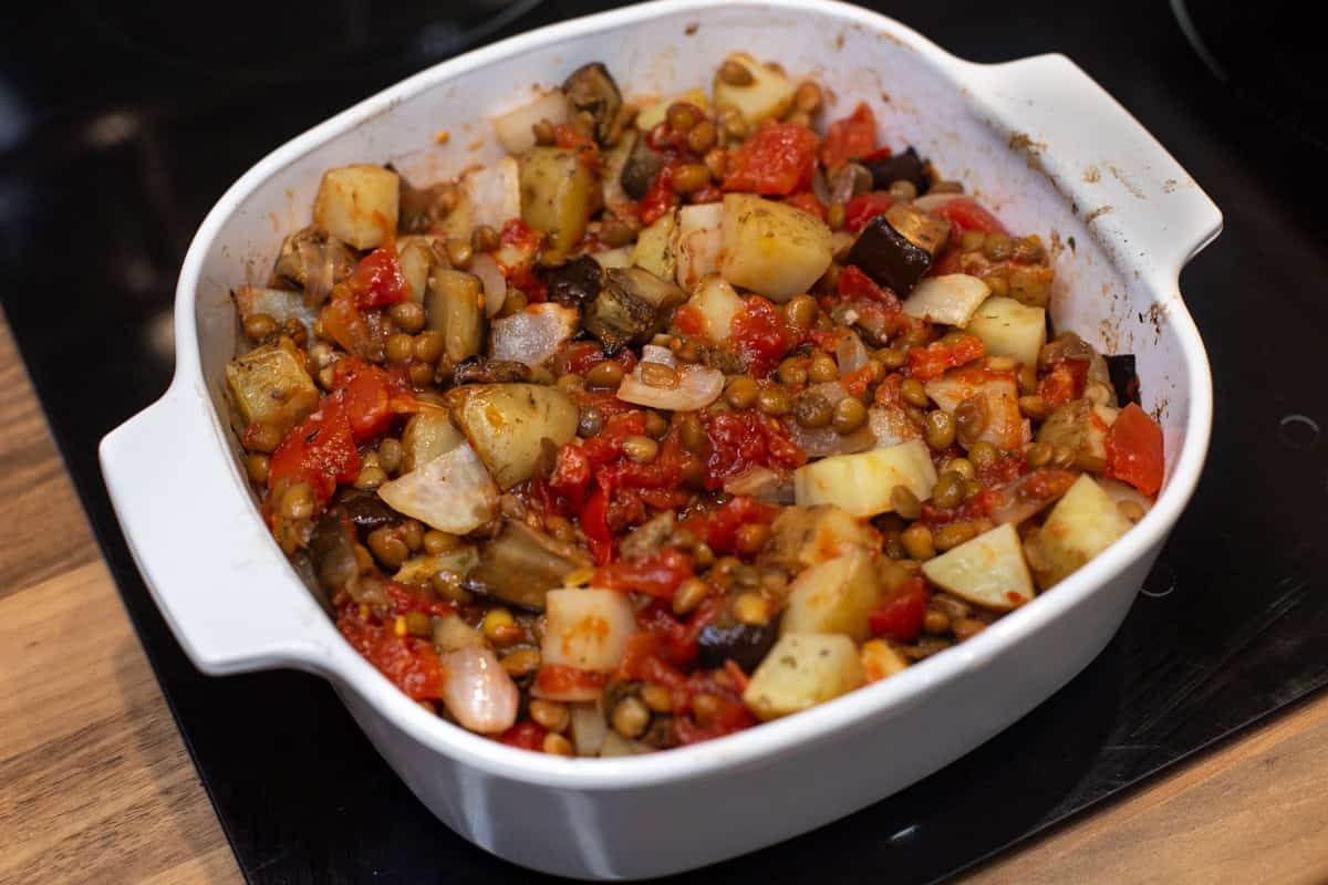 A baking dish with roasted vegetables and lentils in tomato sauce.