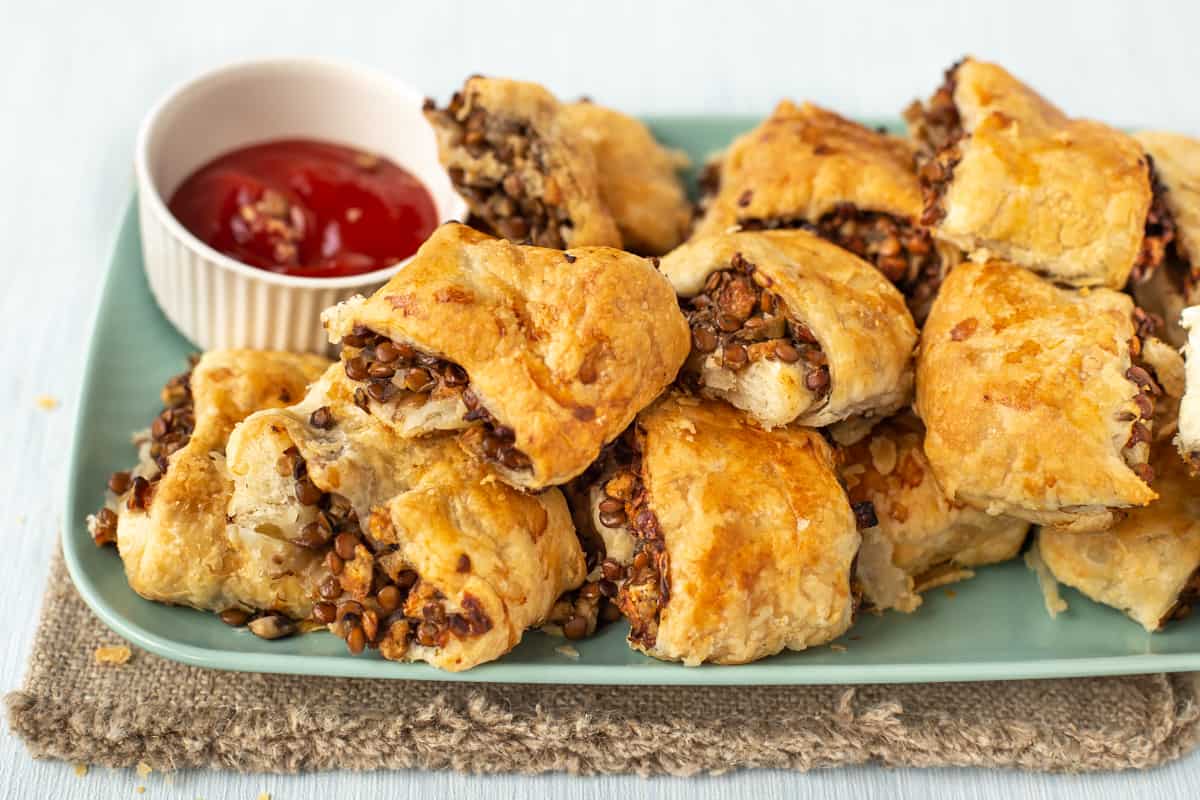 A plate piled up with vegetarian sausage rolls, with a pot of ketchup behind.