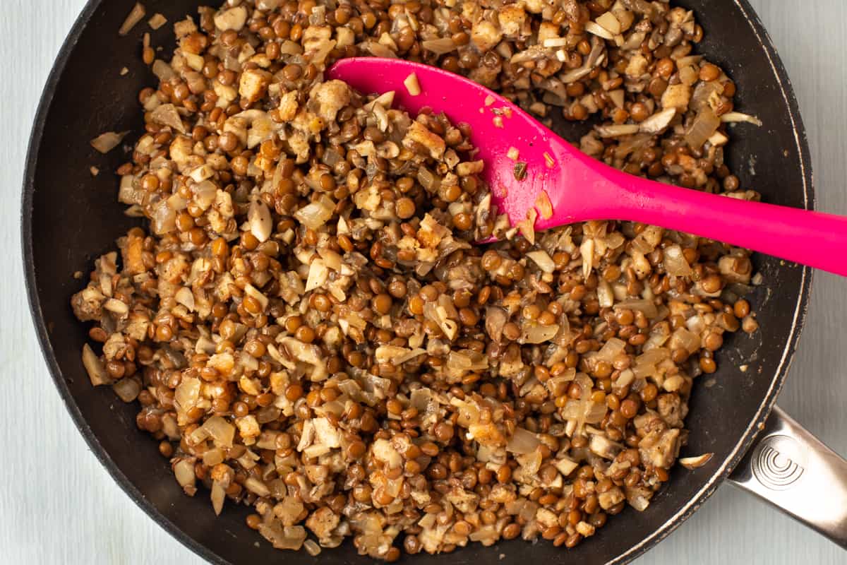 Lentils, onions and mushrooms cooking in a large frying pan.