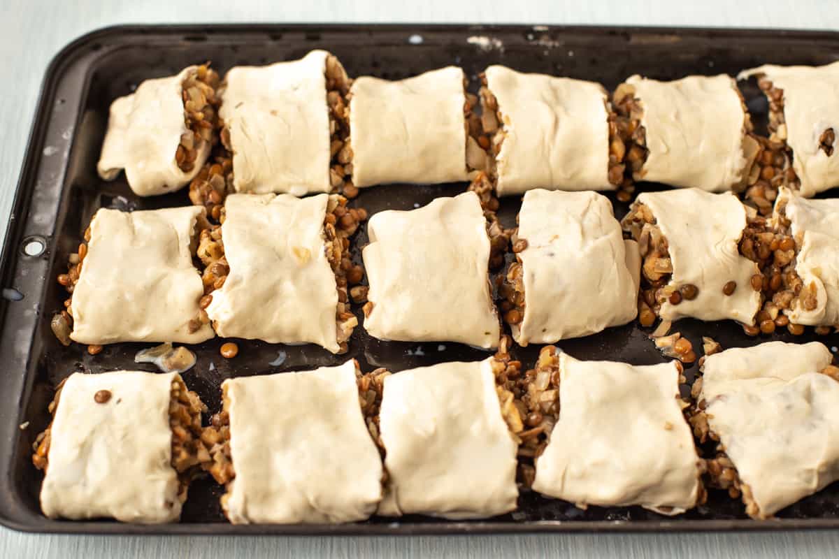 Uncooked vegetarian sausage rolls laid out on a baking tray.