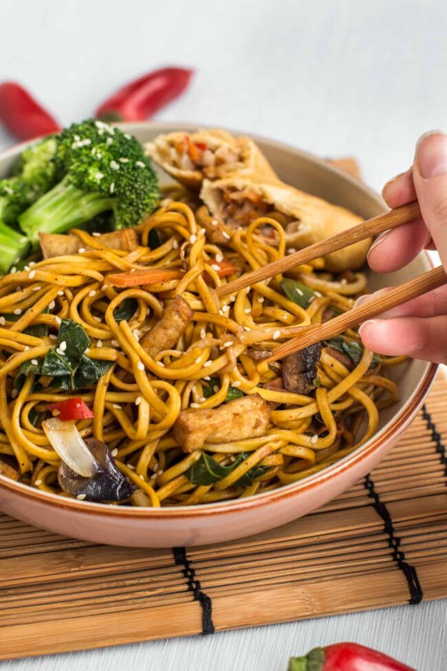 Veggie chow mein being eaten with a pair of chopsticks.