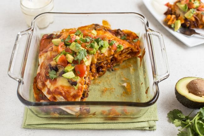 Veggie enchilada stack in a baking dish with a large slice removed