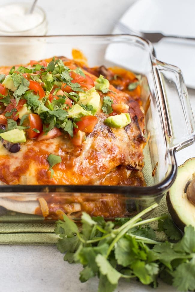 Veggie enchilada stack in a baking dish, topped with avocado and tomatoes
