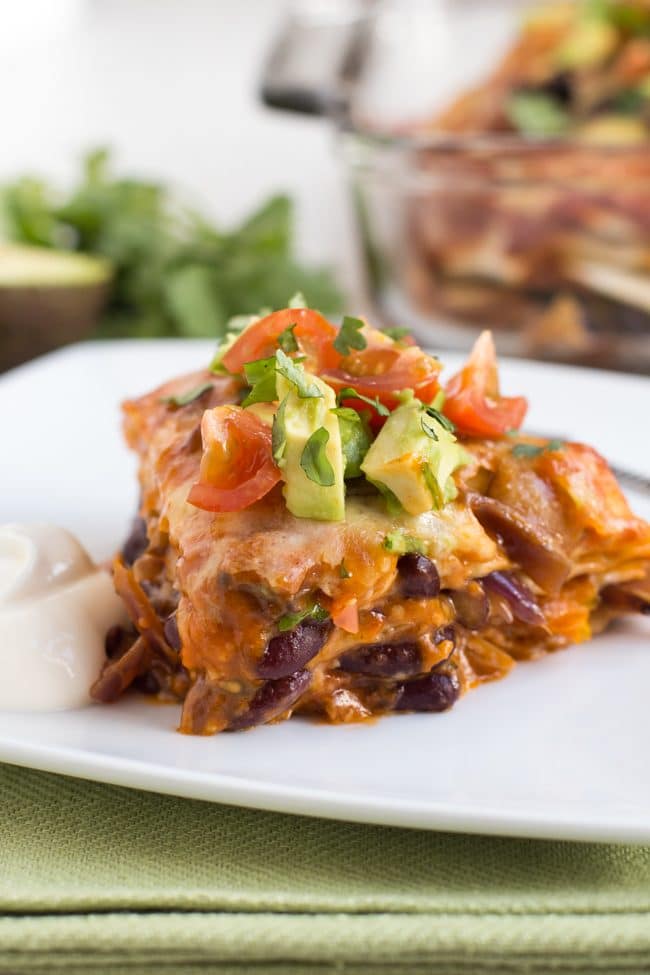 Portion of veggie enchilada stack on a plate topped with avocado and tomatoes