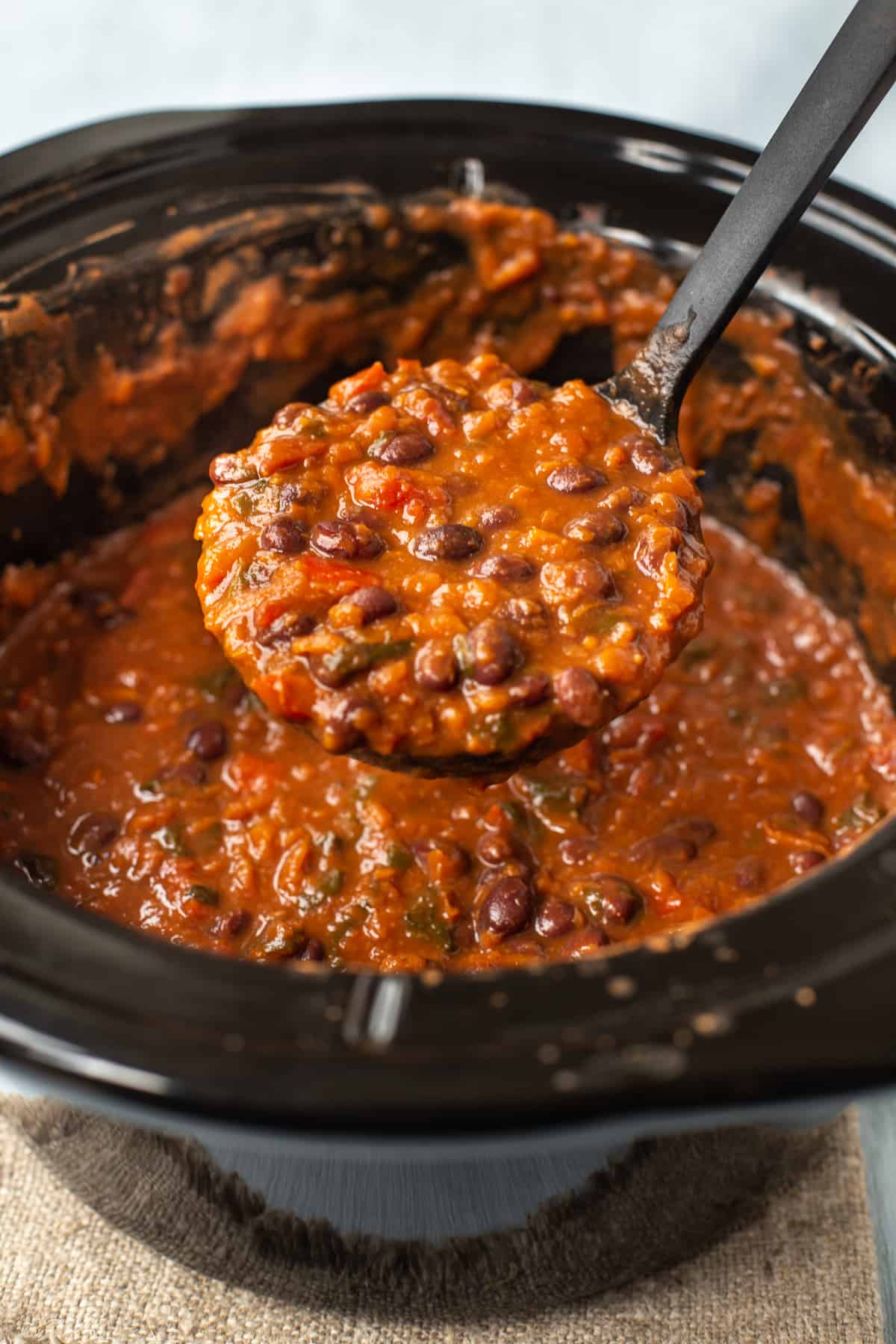 A ladle scooping some black bean soup from a slow cooker.
