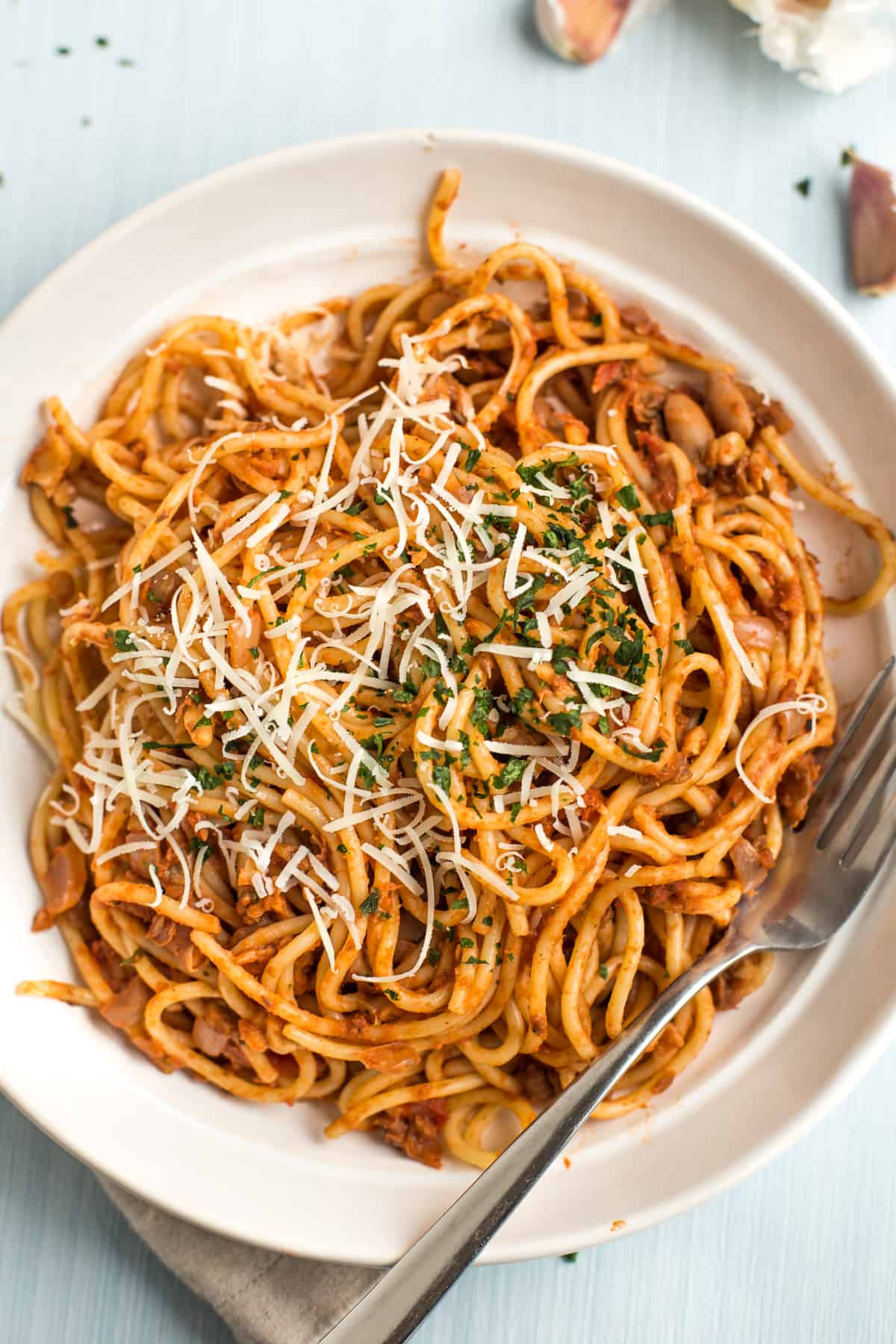 Portion of vegan spaghetti bolognese mixed together in a bowl topped with cheese and parsley.