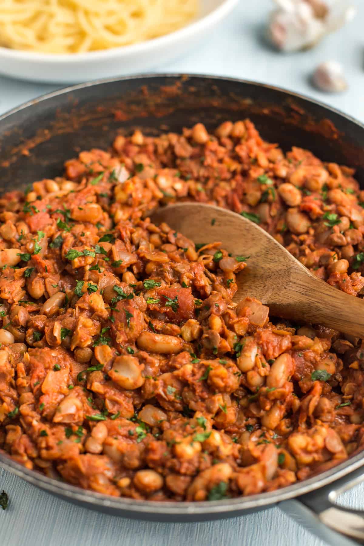 Vegan bolognese sauce in a frying pan with a wooden spoon.