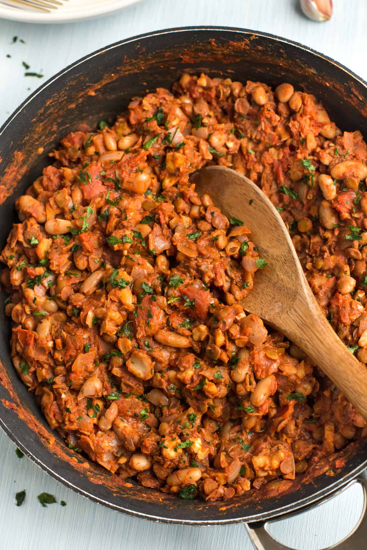 Vegan walnut and bean bolognese in a frying pan with a wooden spoon.