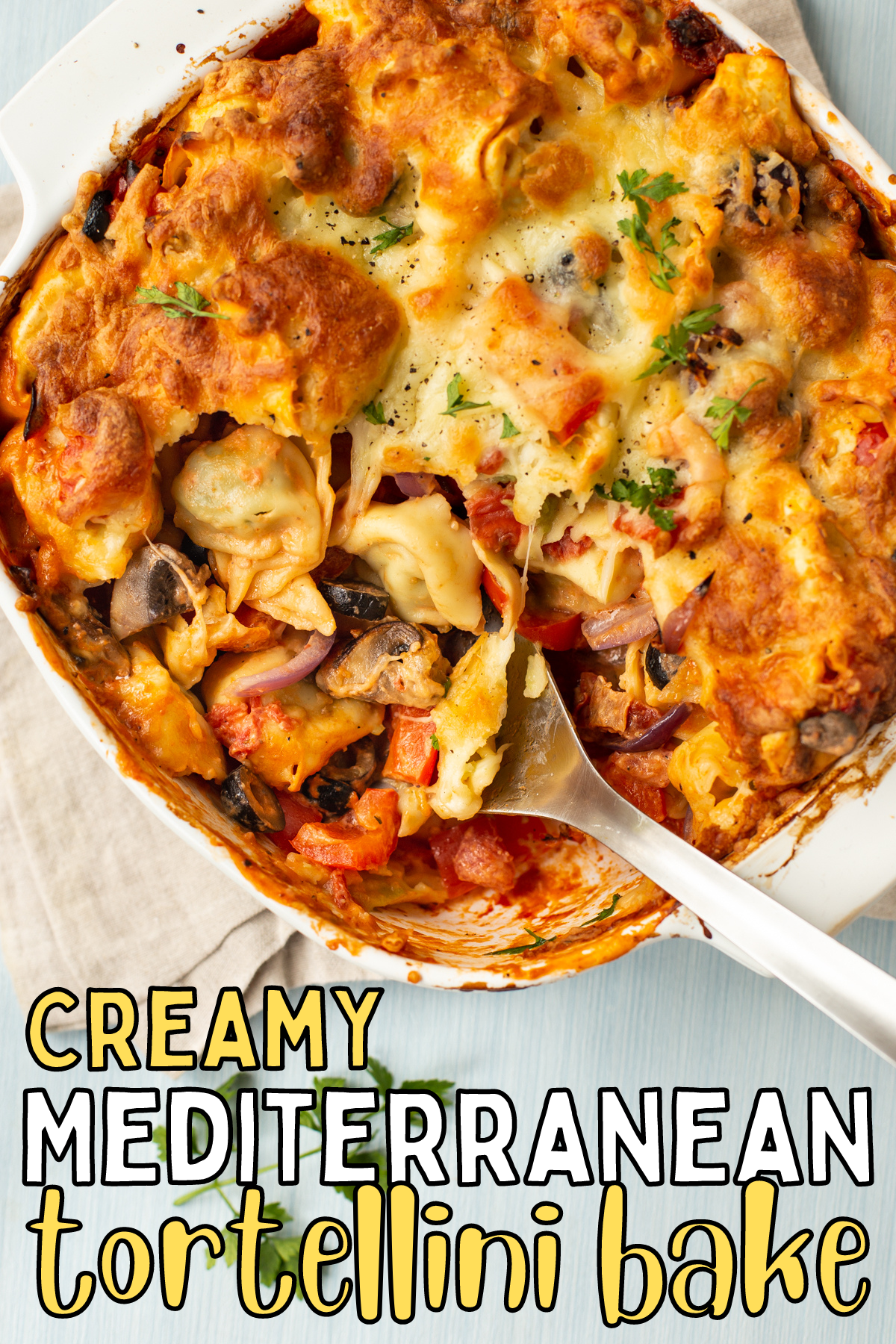 A spoon taking a scoop of tortellini bake from a baking dish.